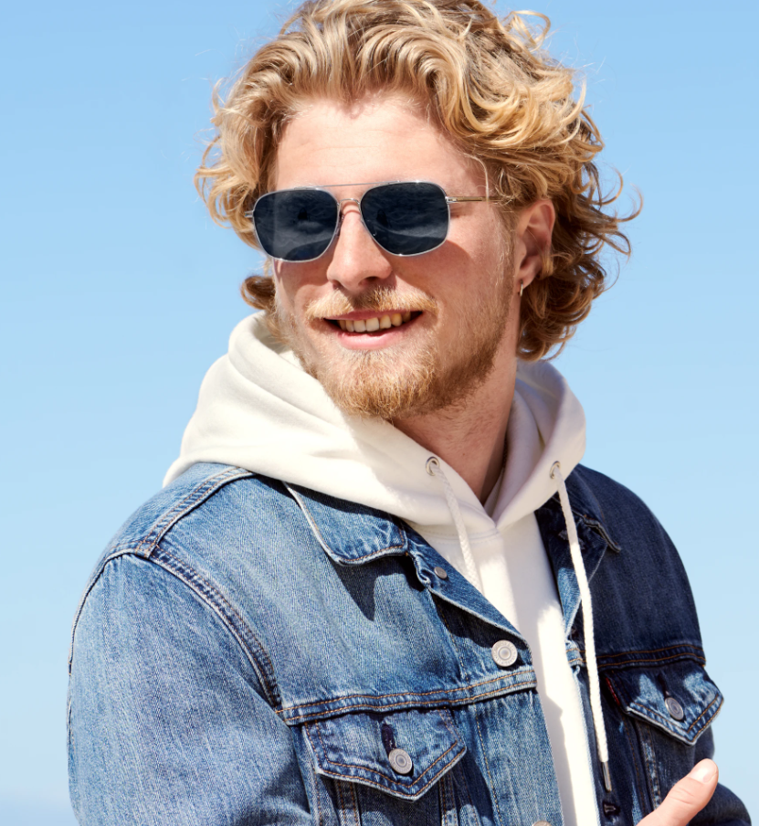 Bărbat poartă ochelari de soare Aviator cu Punte dubla, cu rame argintii și lentile negre, decor luminos de zi, purtând o jachetă jeans și hanorac alb.