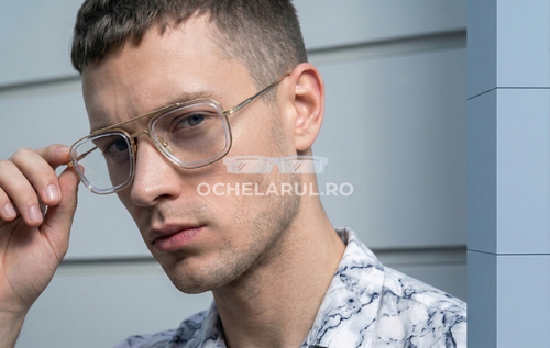 Bărbat purtând ochelari Ochelari Dita Flight Style cu ramă aurie transparentă și lentile transparente în fața unui perete modern.