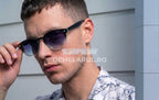 Bărbat purtând ochelari de soare Moscot Lemtosh Style cu rame negre și lentile violet degrade, stil modern.