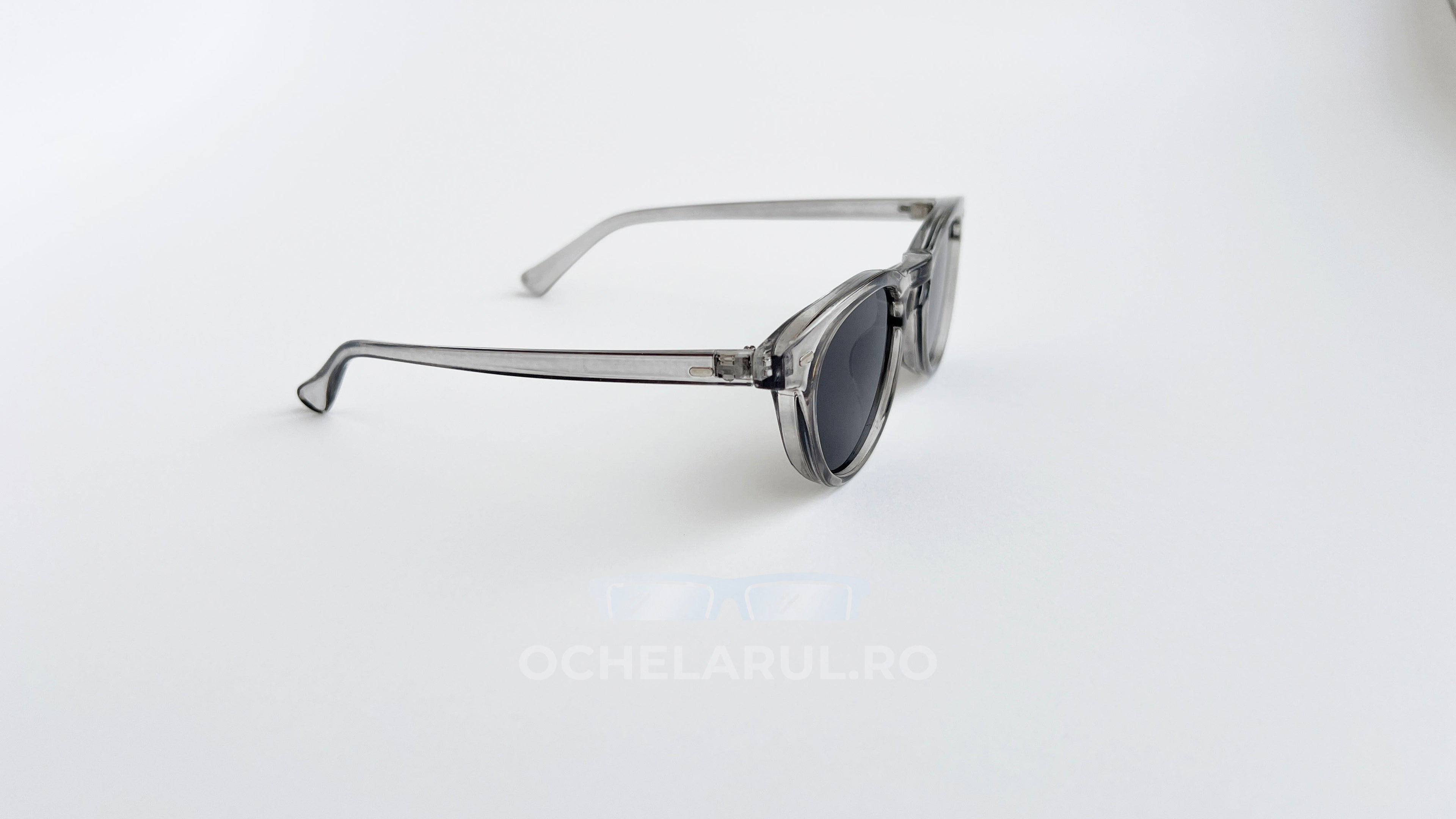 Ochelari de soare Oliver Peoples Style cu rame transparente gri și lentile gri, design modern pentru bărbați.