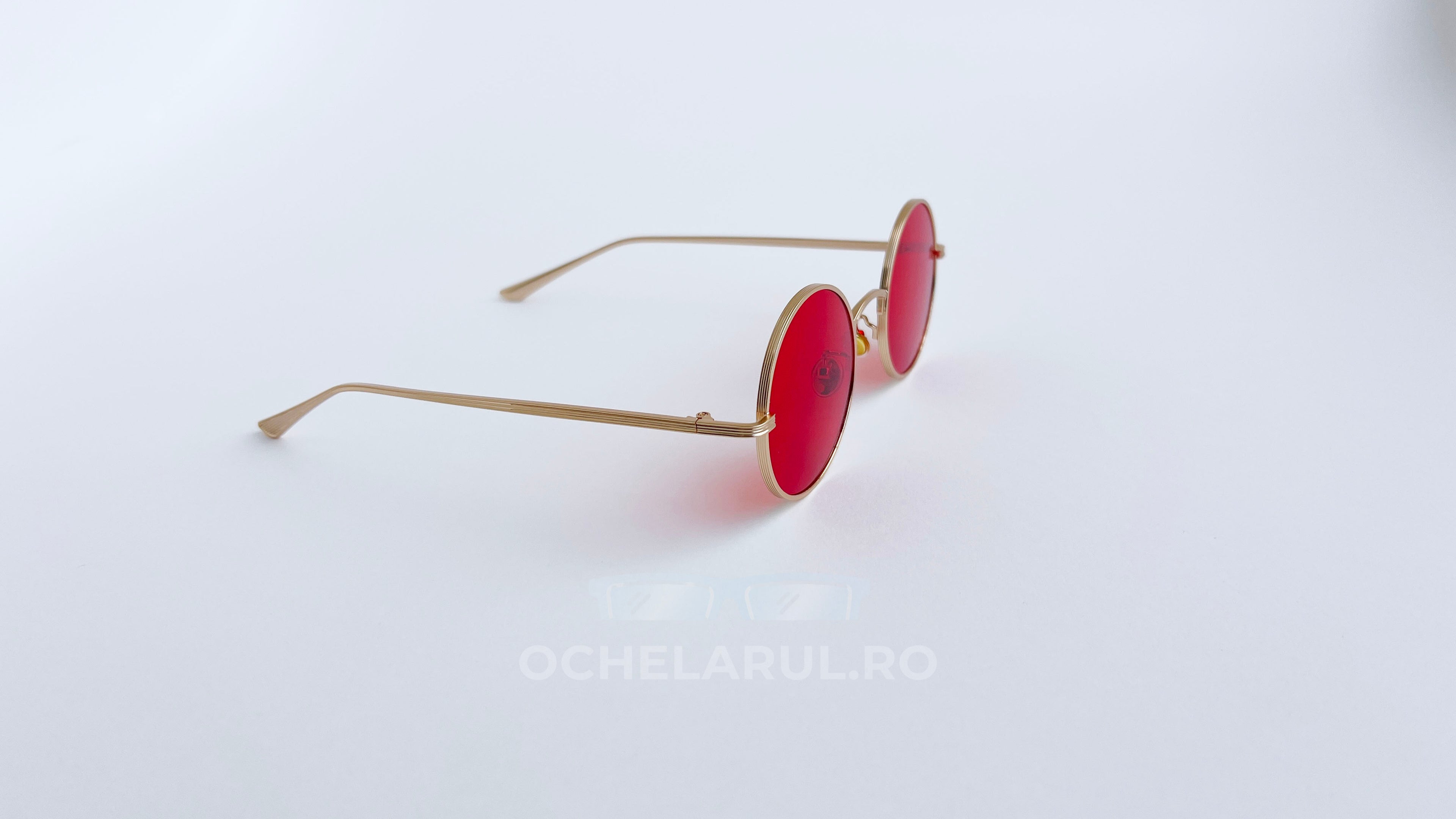 Ochelari de soare Rotunzi cu rame aurii subțiri și lentile roșii, design modern pentru protecție și stil în zilele însorite.