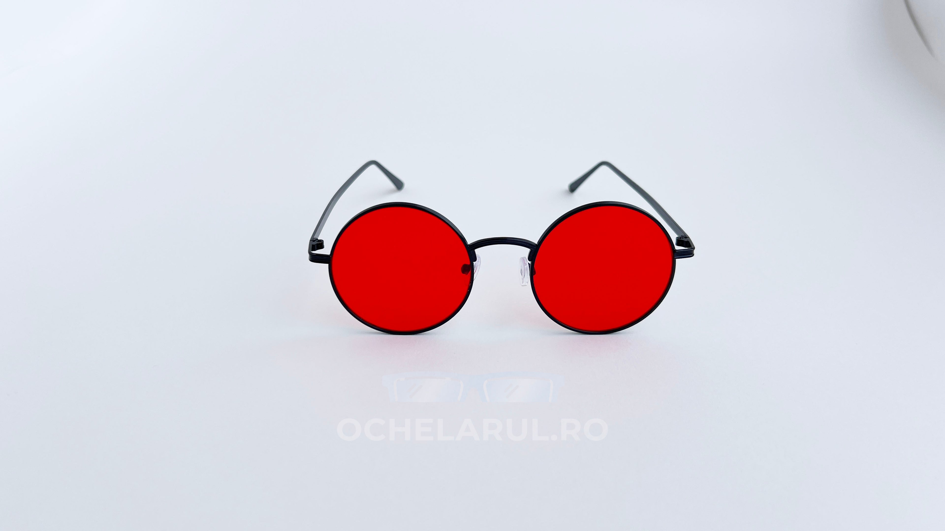 Ochelari de soare Rotunzi cu ramă neagră subțire și lentile roșii intense, design modern și distinctiv.