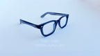 Rame ochelari Moscot Klutz Style în nuanță gri închis, cu lentile transparente, prezentate pe fundal alb.